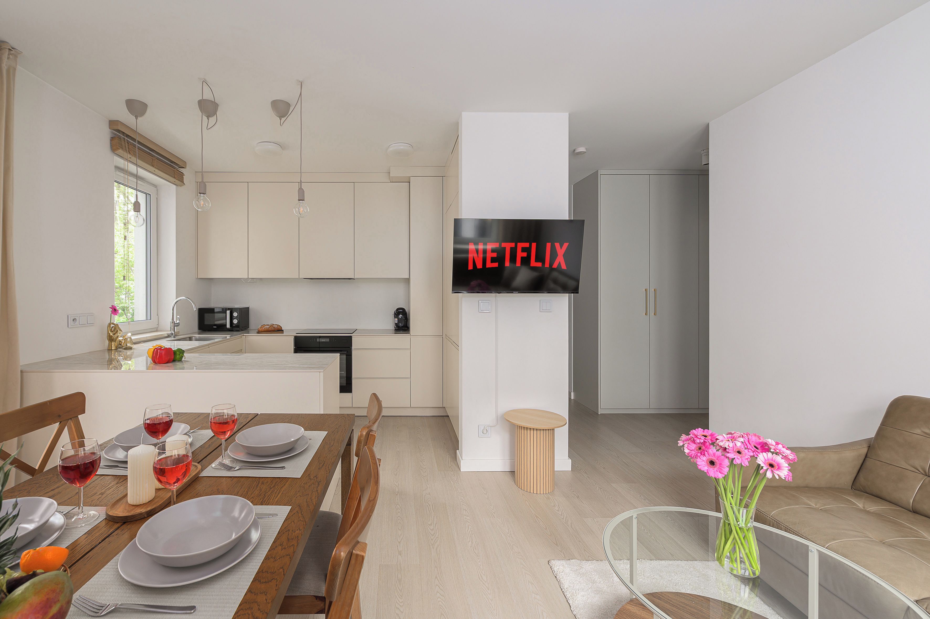 Une cuisine moderne avec un coin repas, un téléviseur à écran plat fixé au mur et un salon comprenant un canapé et un vase de fleurs.