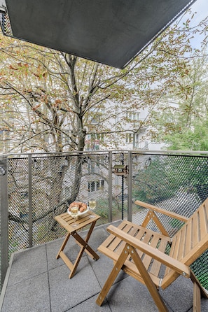 A balcony with a table and two chairs, a tree, and a building in the background. - Lumina 4-room Apart, Parking, Balcony (Warszawa)