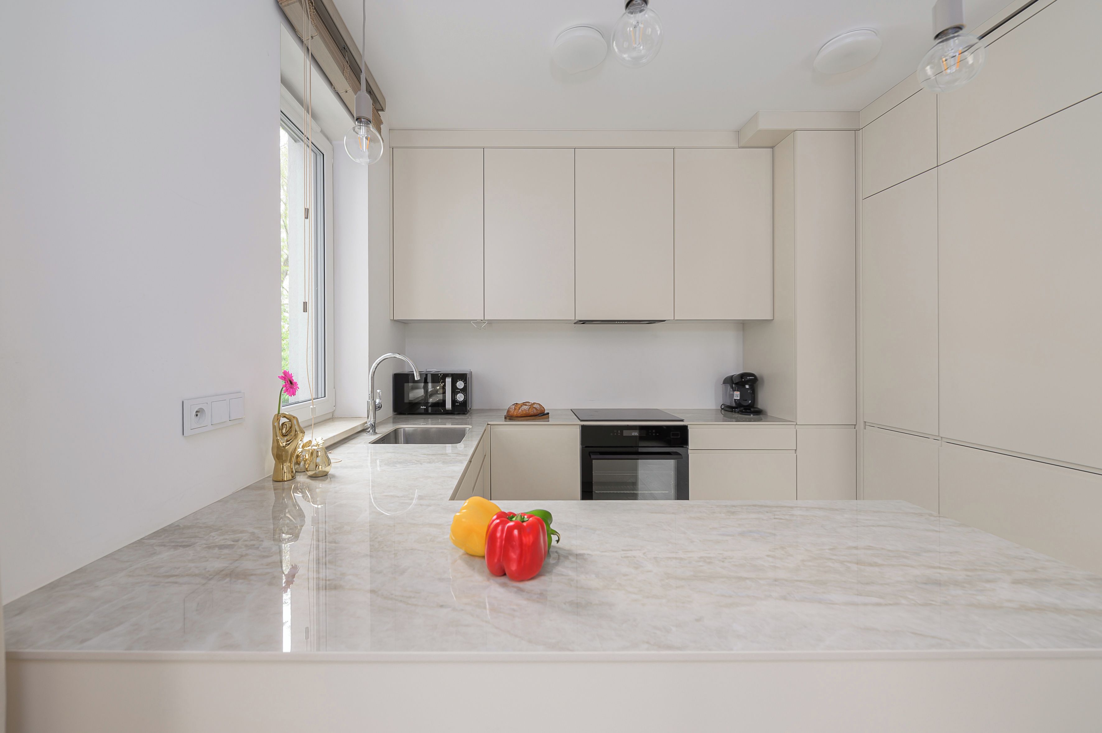A modern kitchen with white cabinets, a marble countertop, and a built-in oven.
