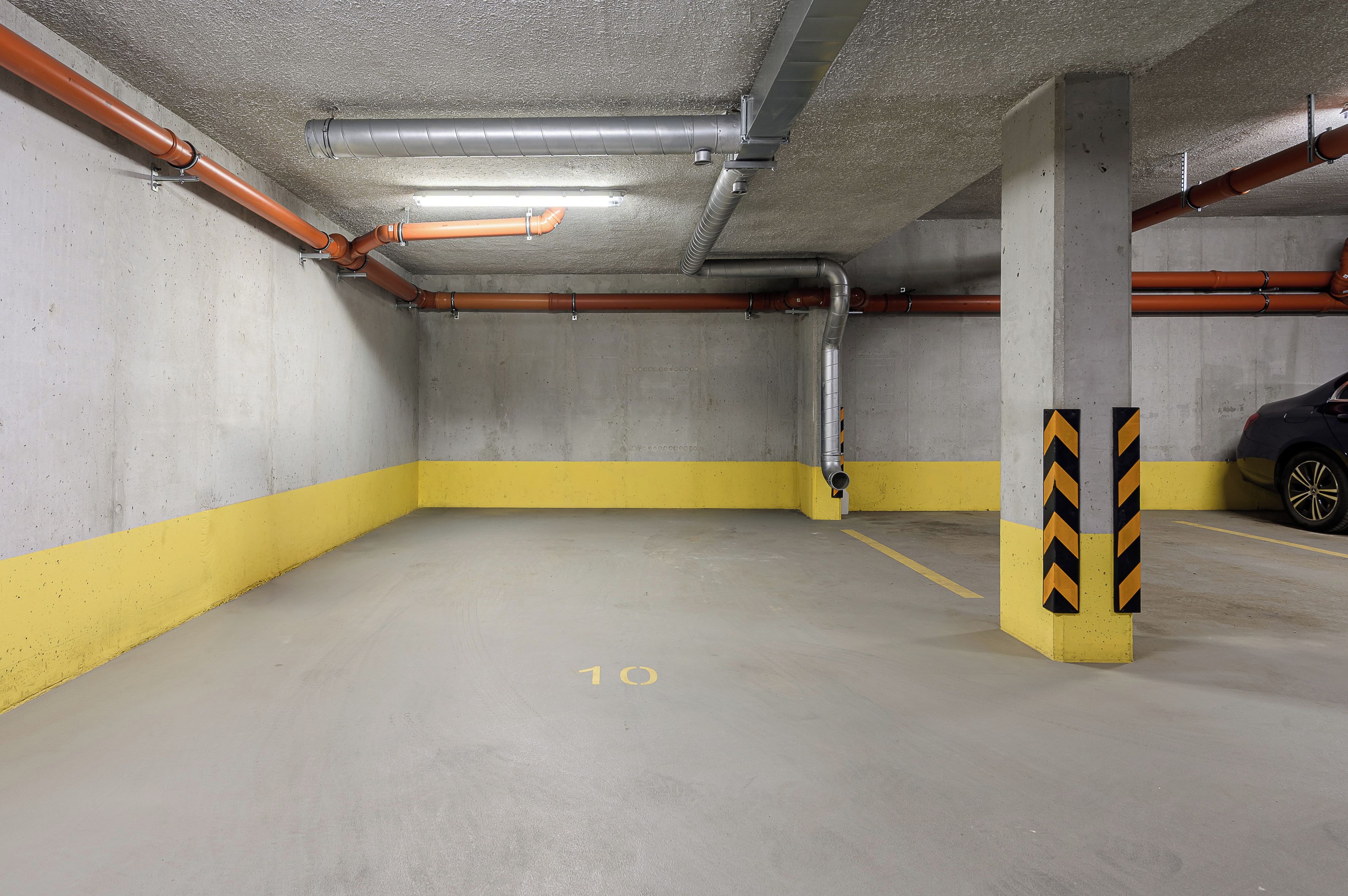 En parkeringskælder med betonvægge, gulv malet i gult og gråt, og flere parkeringspladser.