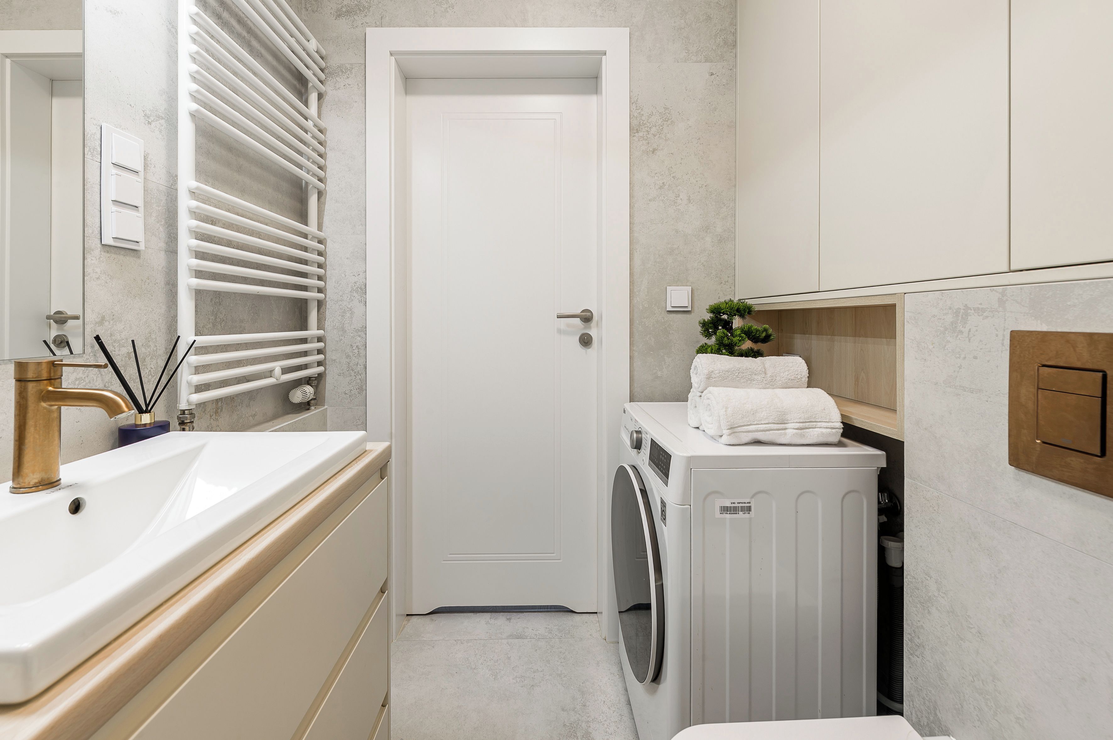 A modern bathroom with a white sink, a washing machine, and a door.