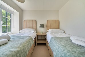 Un dormitorio con dos camas, una mesita de noche con lámpara y ventana con vista a árboles.