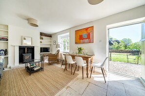 Un amplio salón con chimenea, comedor con mesa y sillas, televisor y un gran ventanal con vistas al exterior.