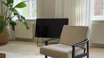 A living room with a large window, a television, a beige armchair, a zebra-patterned ottoman, and a potted plant.