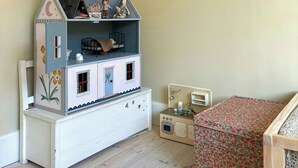 Et værelse med et dokkehjem, en bogreol fyldt med børnebøger og en kommode med blomstermønster.