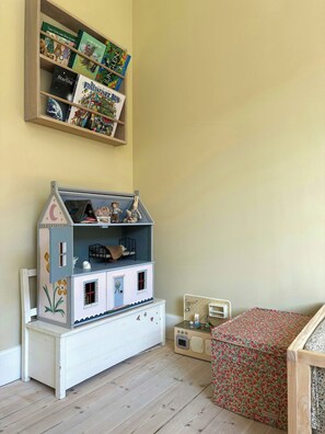 Quarto com uma casa de bonecas, uma estante de livros infantis e uma cômoda com padrão floral.