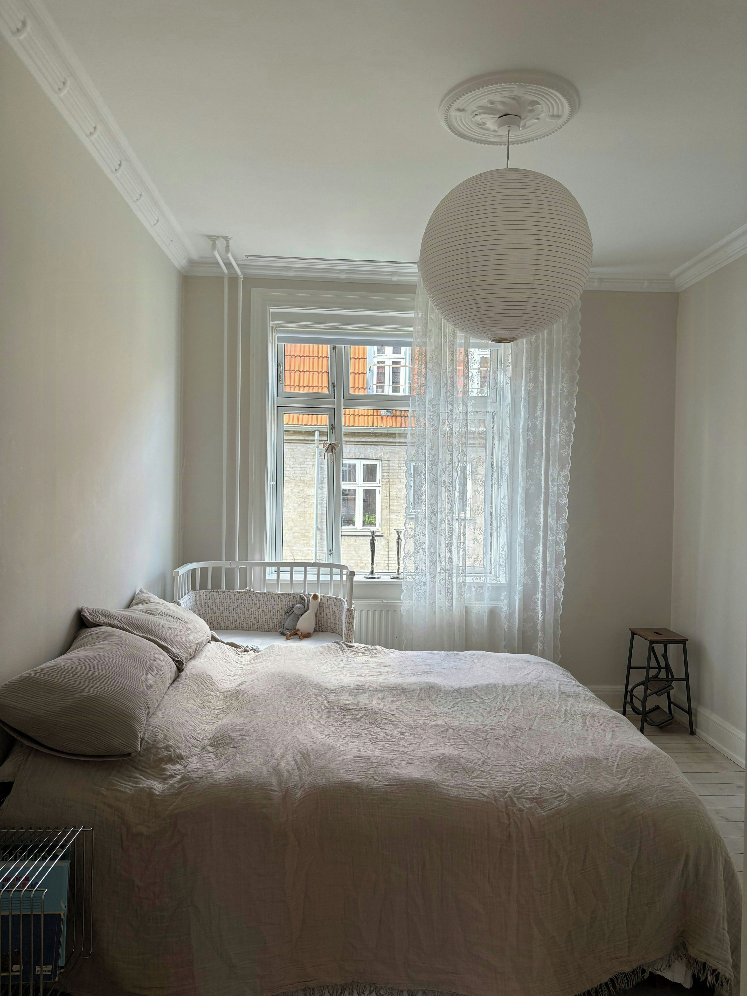 A bedroom with a large bed, a crib, a standing lamp, and a window with curtains.