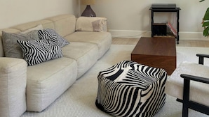 En stue med en beige sofa, puder med zebra-mønster, et træsofabord og en vægmonteret skulptur.