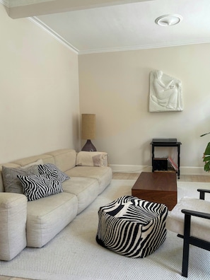 Sala de estar com sofá bege, almofadas com padrão de zebra, mesa de centro de madeira e uma escultura na parede.