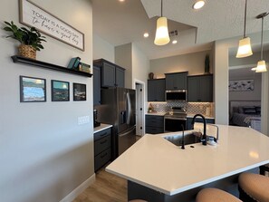A modern kitchen with a central island, dark cabinets, stainless steel appliances, pendant lighting, and a motivational quote on the wall. - Mesquite 3BR Home | Private Pool + Slide | Free Activities | Views (Mesquite)