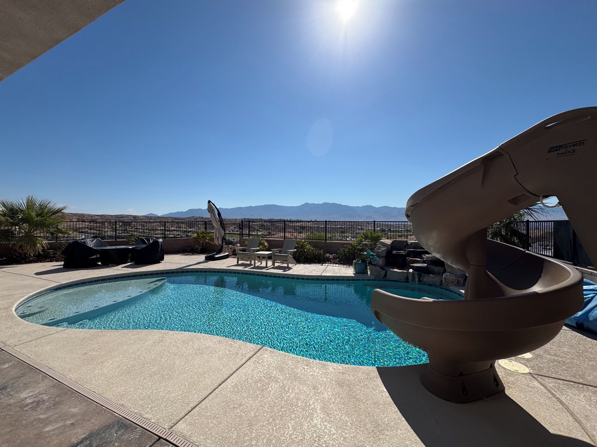 A swimming pool with a slide, lounge chairs, and a view of mountains.