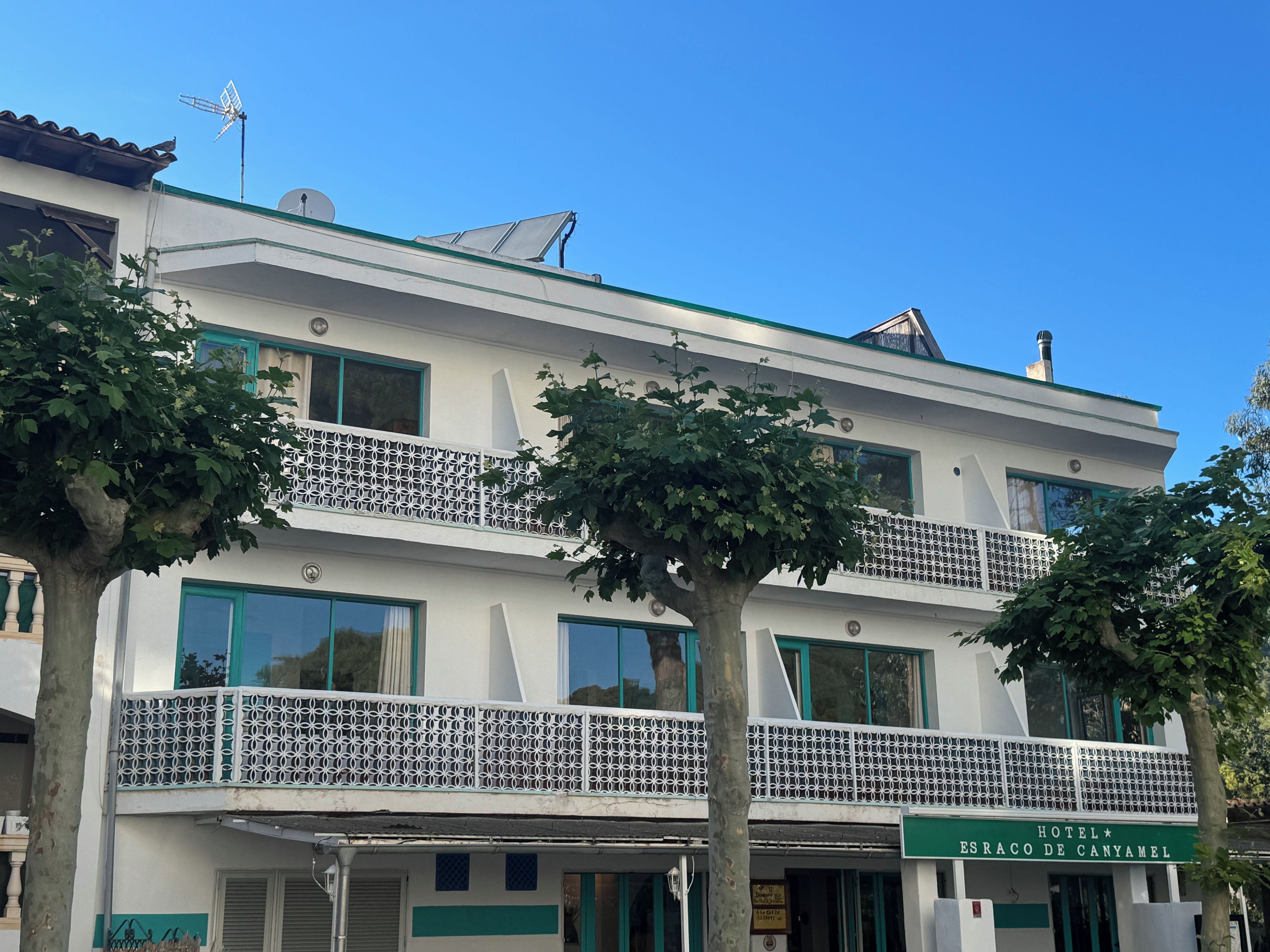 Un hotel de dos pisos con balcones, un cartel que indica que es el 'Hotel Esraco de Canyamel', y un cielo azul despejado.