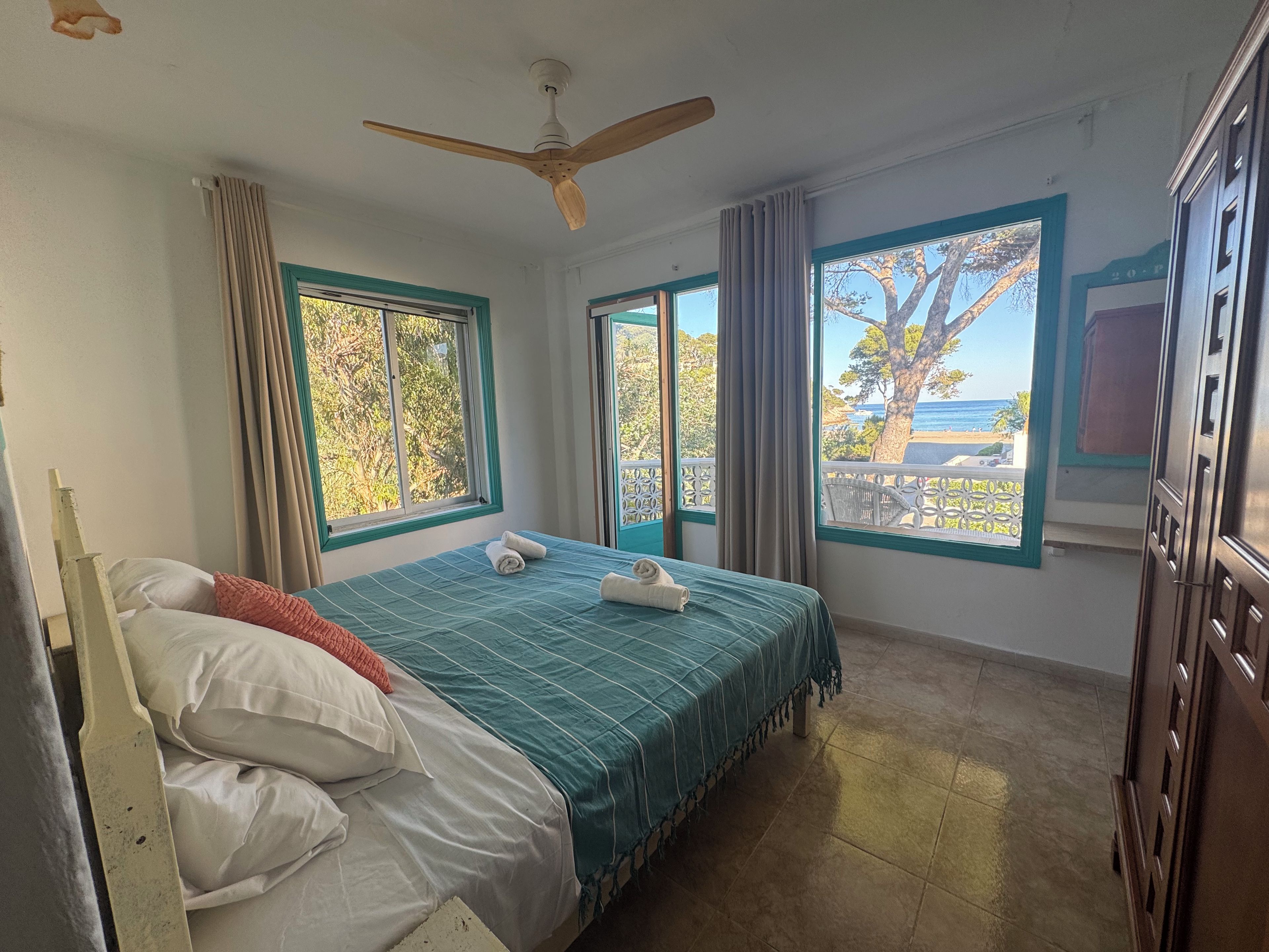 Un dormitorio con cama, ventilador de techo y vistas al exterior.