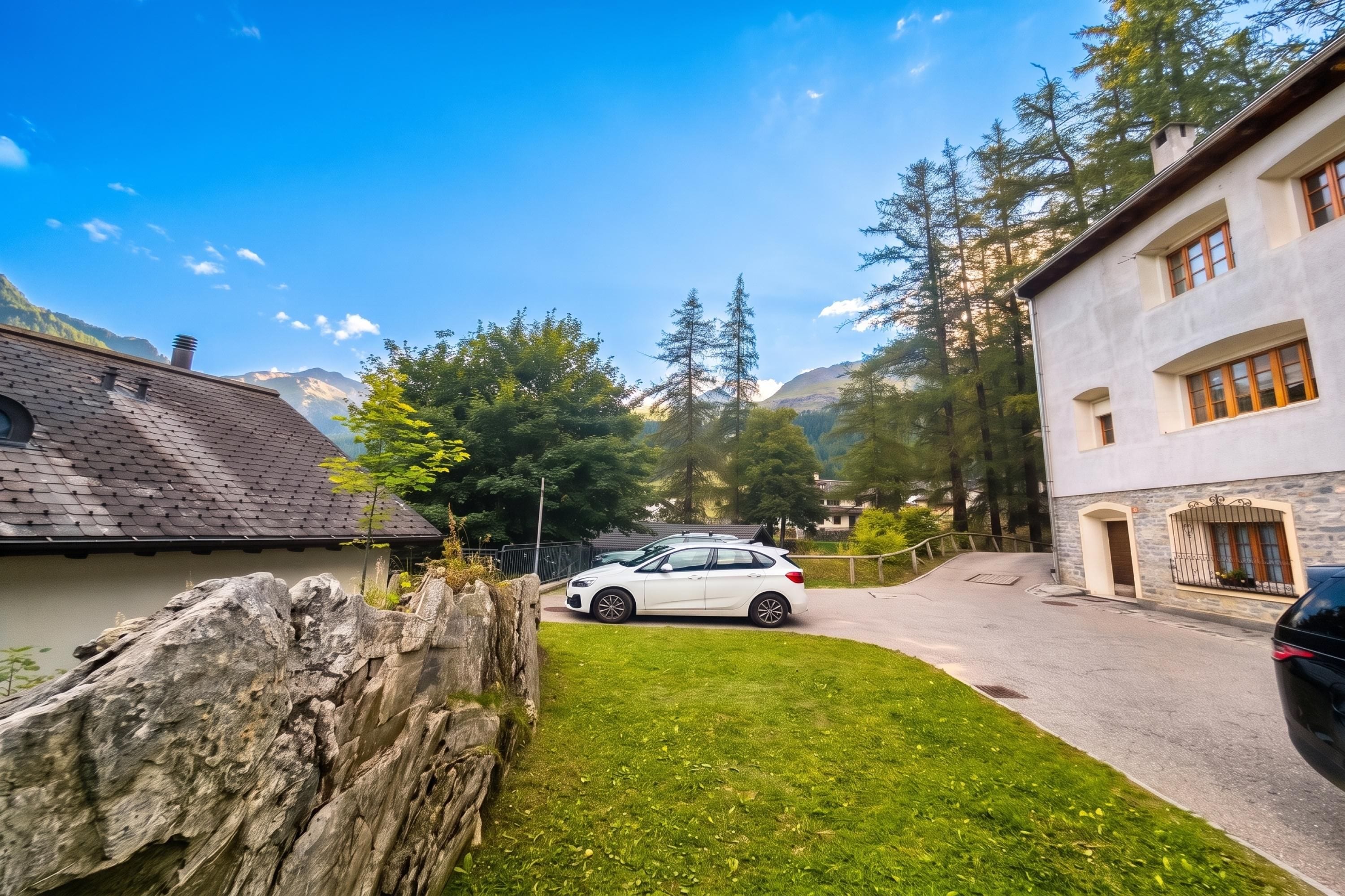 Un quartier résidentiel avec une voiture blanche garée dans l’allée, entouré d’arbres et avec une montagne en arrière-plan.