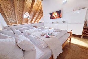 Ein Schlafzimmer mit Holzboden, einem Bett mit weißer Bettwäsche, einer Zeitschrift auf dem Bett, einem Fernseher an der Wand und einer weißen Kommode.