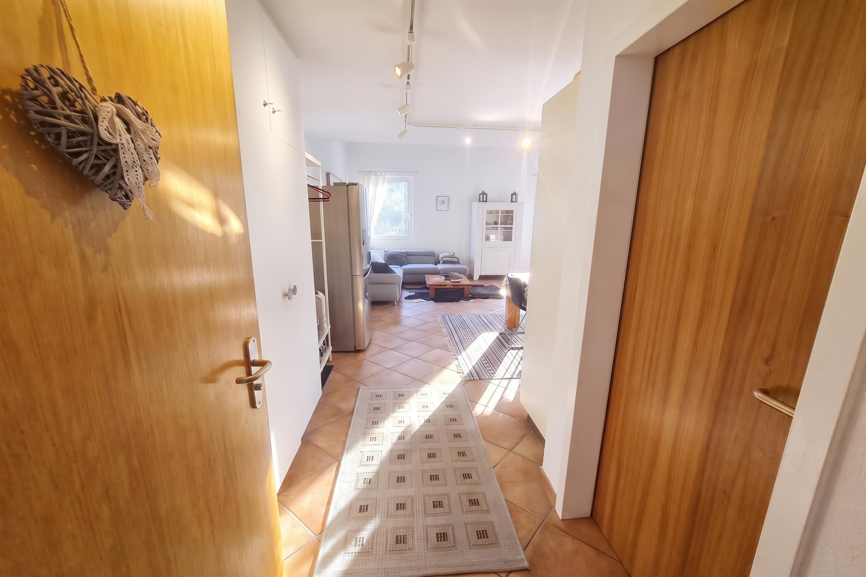 Un couloir mène à un espace de vie comprenant un canapé, un tapis et un meuble.
