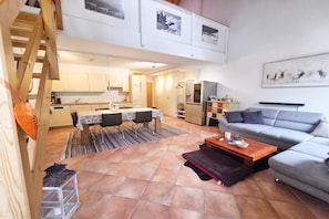 Un ambiente moderno con zona pranzo, cucina e un divano grigio.