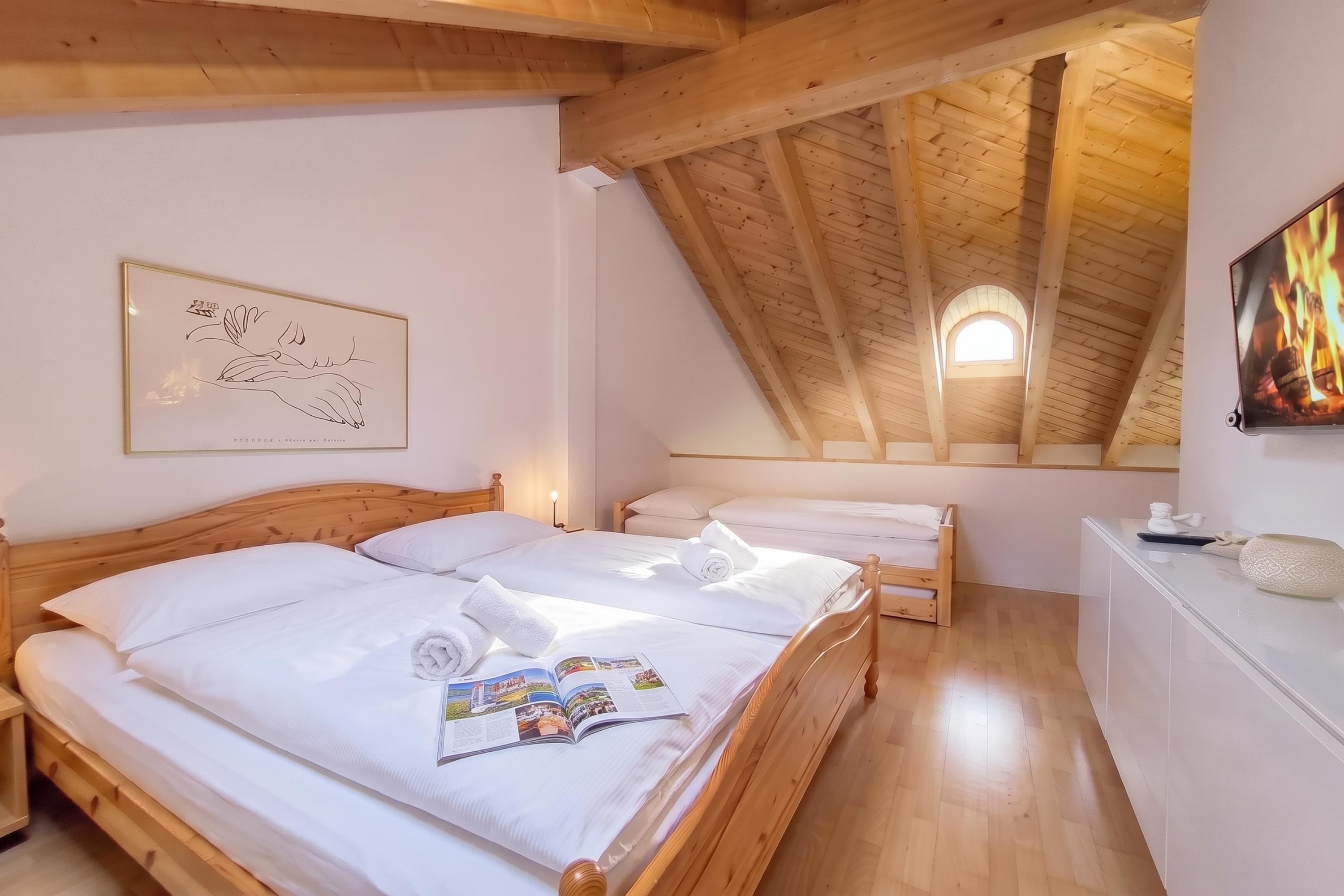 A bedroom with two wooden beds, a wooden ceiling, a wall-mounted TV, and a framed artwork.