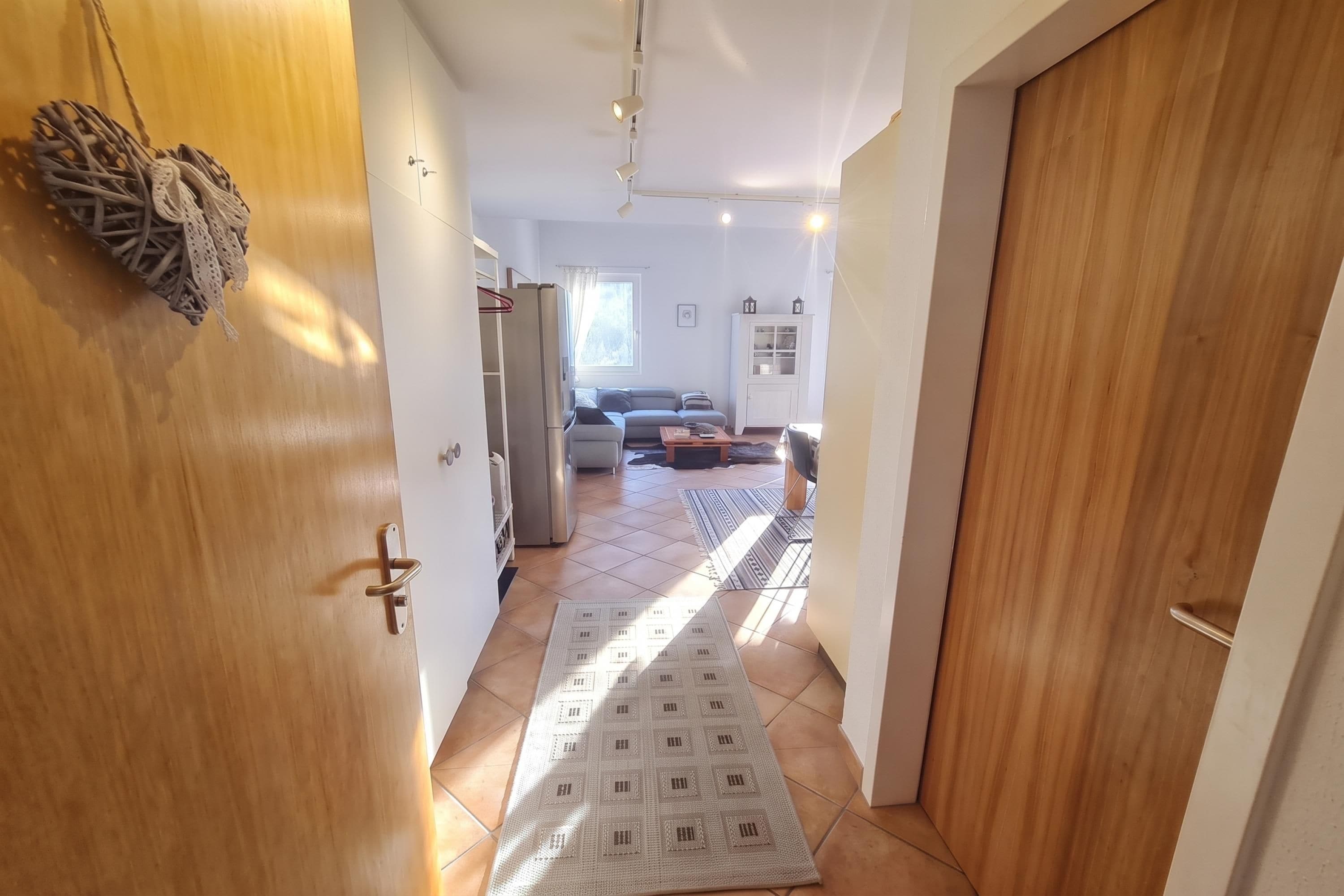 A hallway leading to a living area with a sofa, a rug, and a refrigerator.