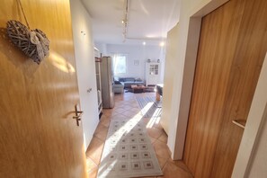Ein Flur, der in einen Wohnbereich mit Sofa, Teppich und Kühlschrank führt.