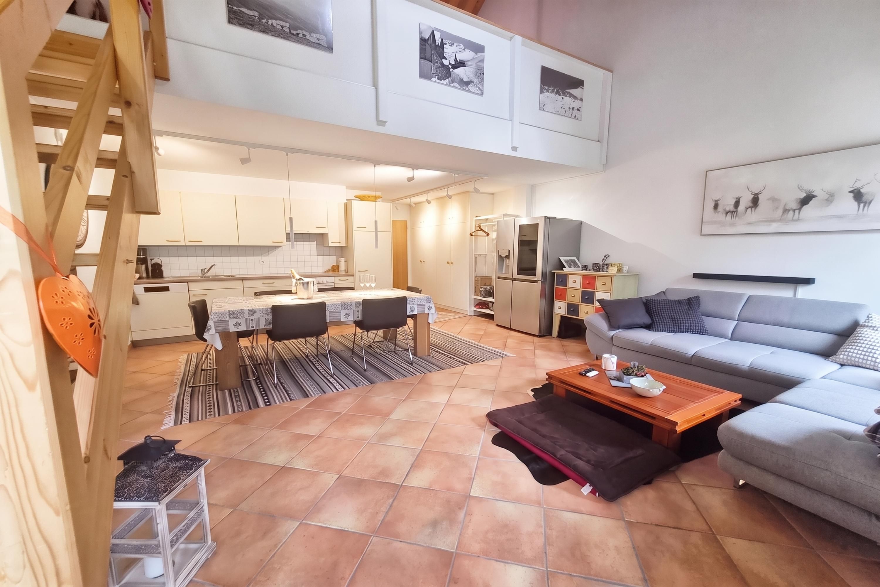 Un vaste espace de vie comprenant un canapé gris, une table basse en bois et un coin repas avec une table dressée pour quatre personnes.