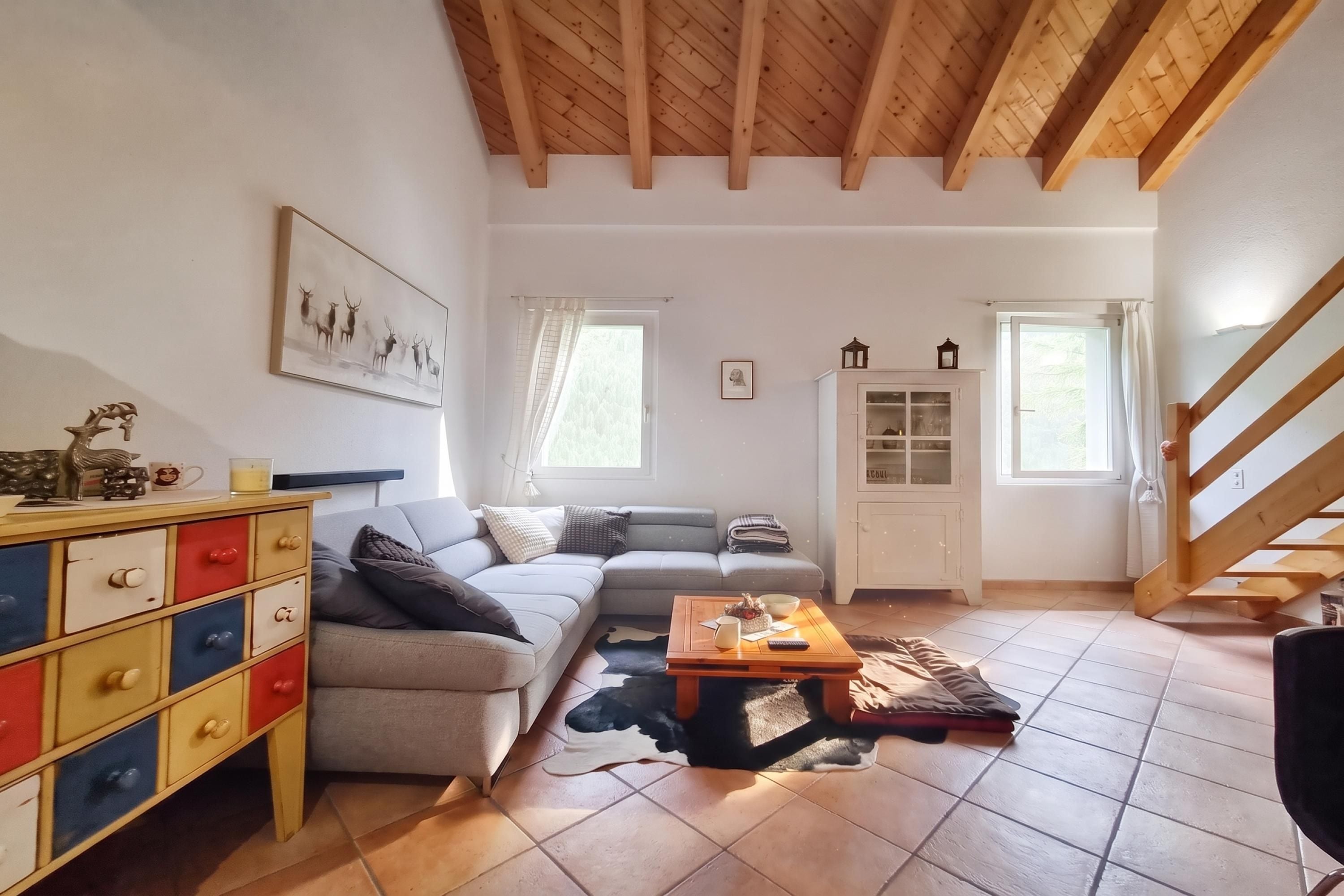 A cozy living room with a sofa, a coffee table, a colorful cabinet, and a staircase.