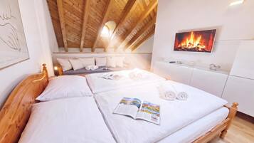 A bedroom with a wooden ceiling, a bed with white linens, a magazine, and a fireplace on the wall.