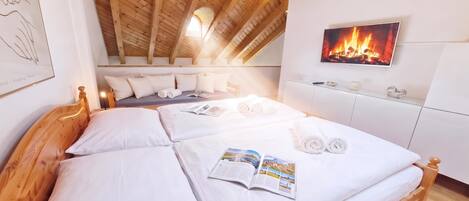 A bedroom with a wooden ceiling, a bed with white linens, a magazine, and a fireplace on the wall.