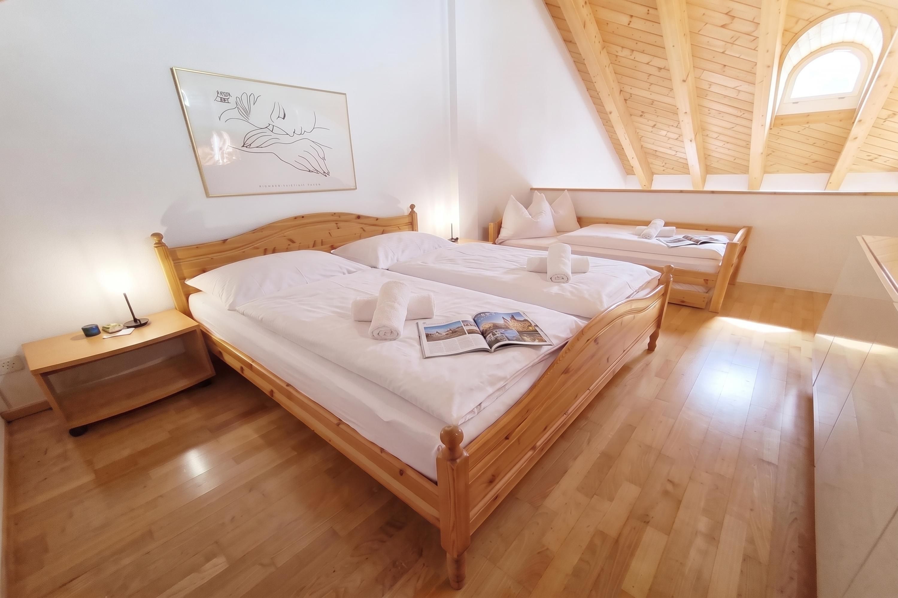 Une chambre à coucher avec deux lits en bois, une table de chevet, un tableau encadré au mur et une lucarne.