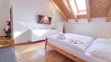 Une chambre avec un plafond en bois, un lit recouvert de draps blancs, un téléviseur à écran plat et une petite commode blanche.