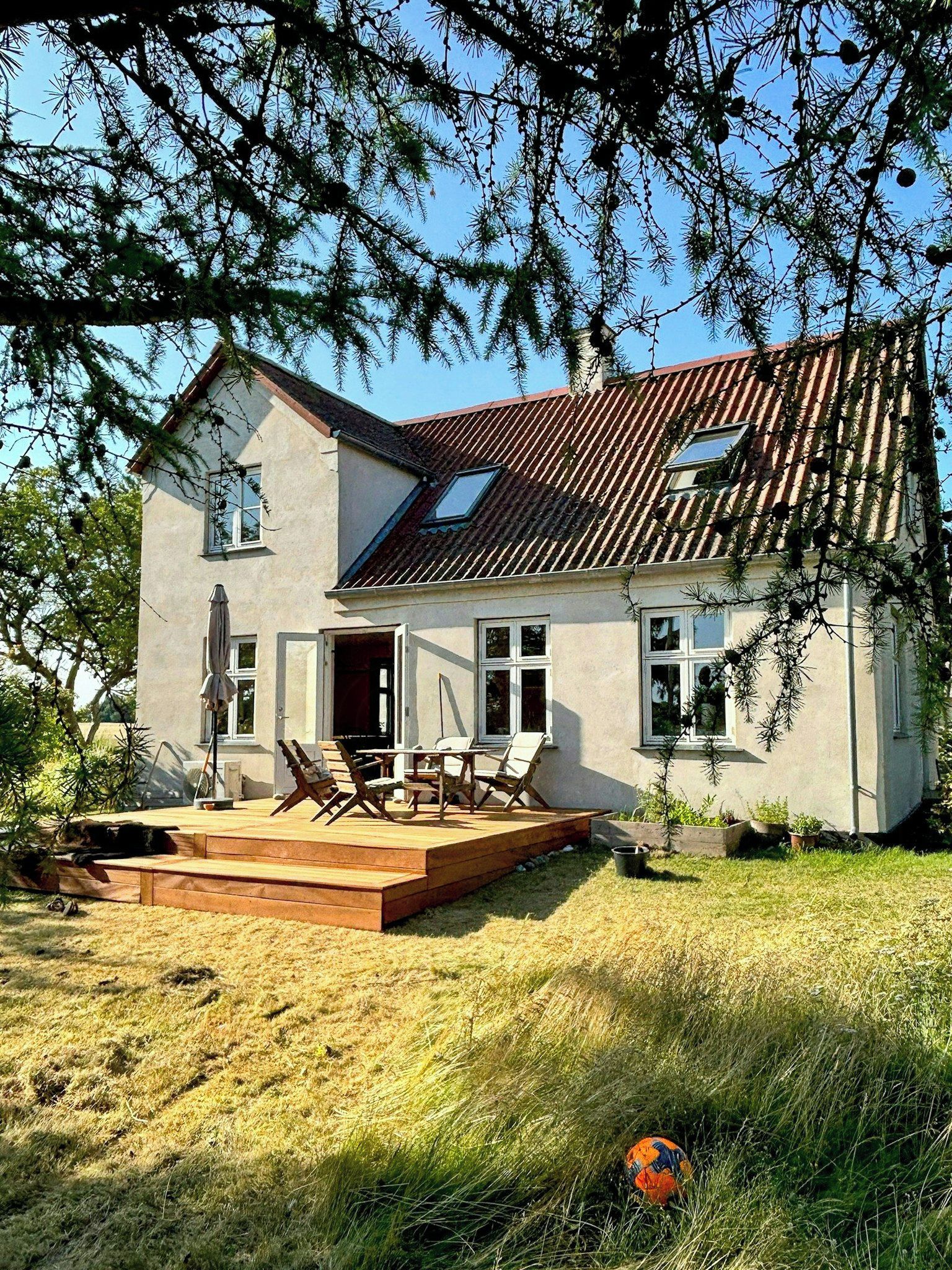 A two-story house with a sloped roof, a patio with outdoor furniture, and a lawn.