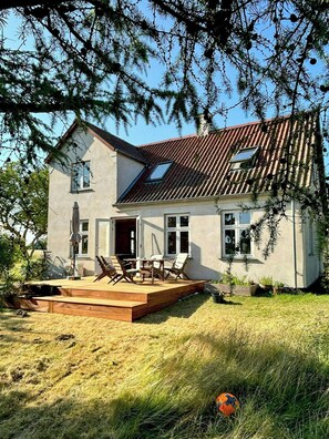 Een huis met twee verdiepingen, een schuin dak, een terras met tuinmeubels en een gazon.