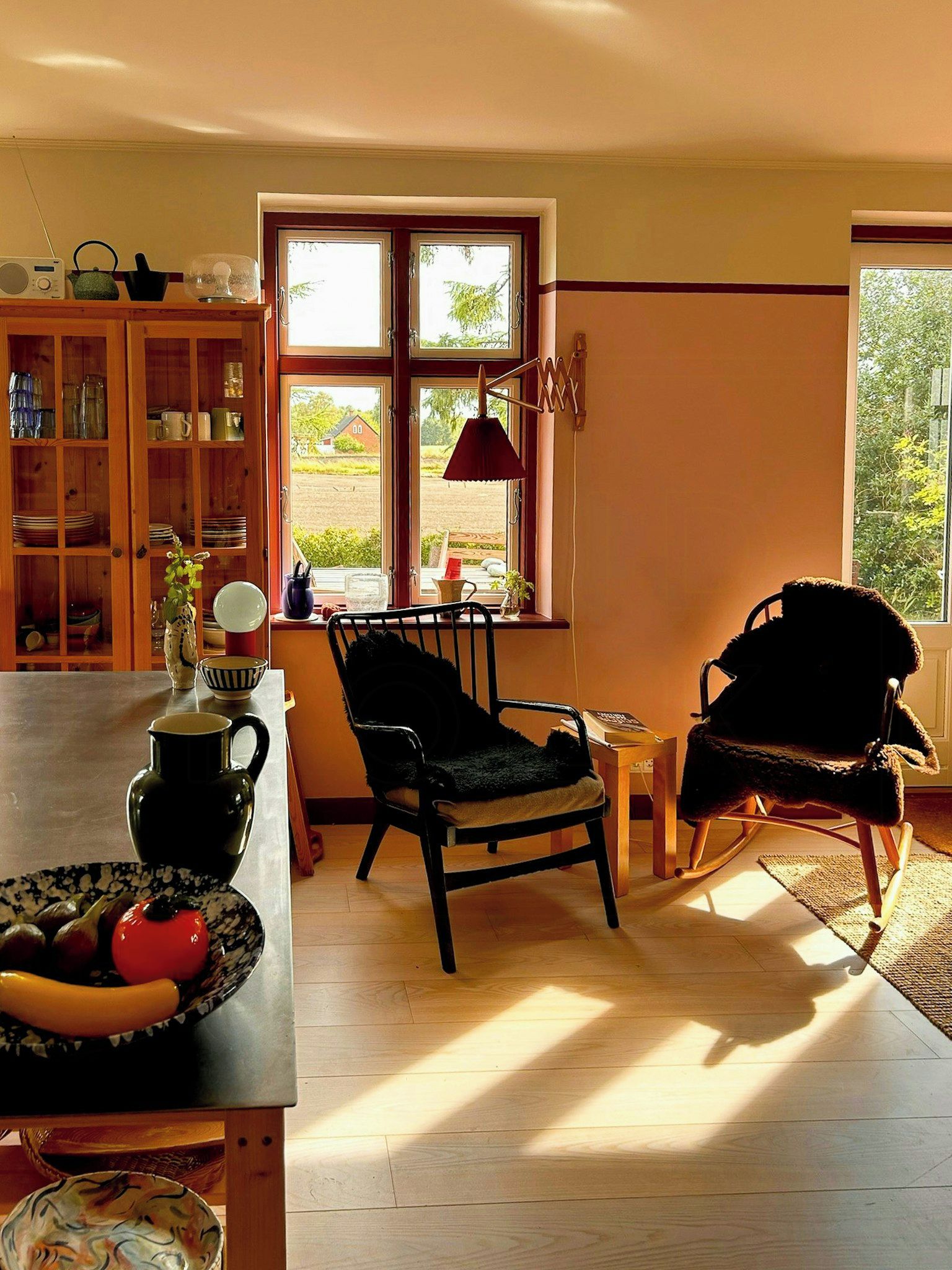 A cozy living room with a wooden table, two chairs, a bookshelf, and a large window.