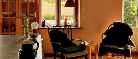 A cozy living room with a wooden table, two chairs, a bookshelf, and a large window.