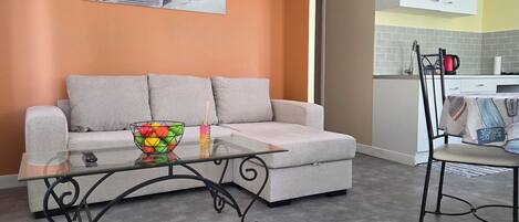 Una sala de estar con un sofá, una mesa de centro de vidrio y un frutero lleno de frutas de colores.