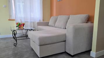 A modern living room with a beige sectional sofa, a glass coffee table, and a small side table.