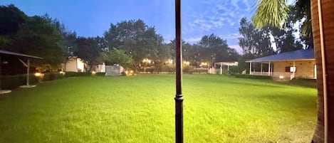 A well-lit grassy area with a lamp post, surrounded by trees and a building structure.