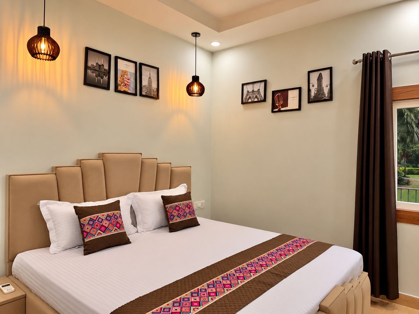 A hotel room with a large bed, multiple pillows, a bedside table with a phone, and framed pictures on the wall.
