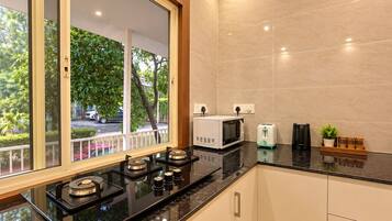 A modern kitchen with a gas stove, microwave, toaster, and a view of a street with trees and parked cars.