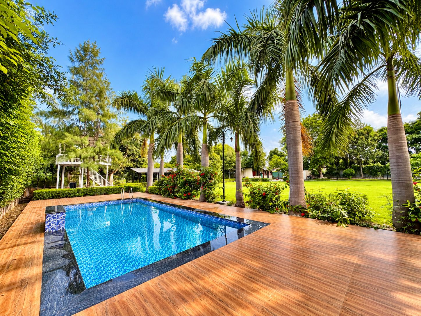 A swimming pool with a wooden deck, surrounded by palm trees and greenery.