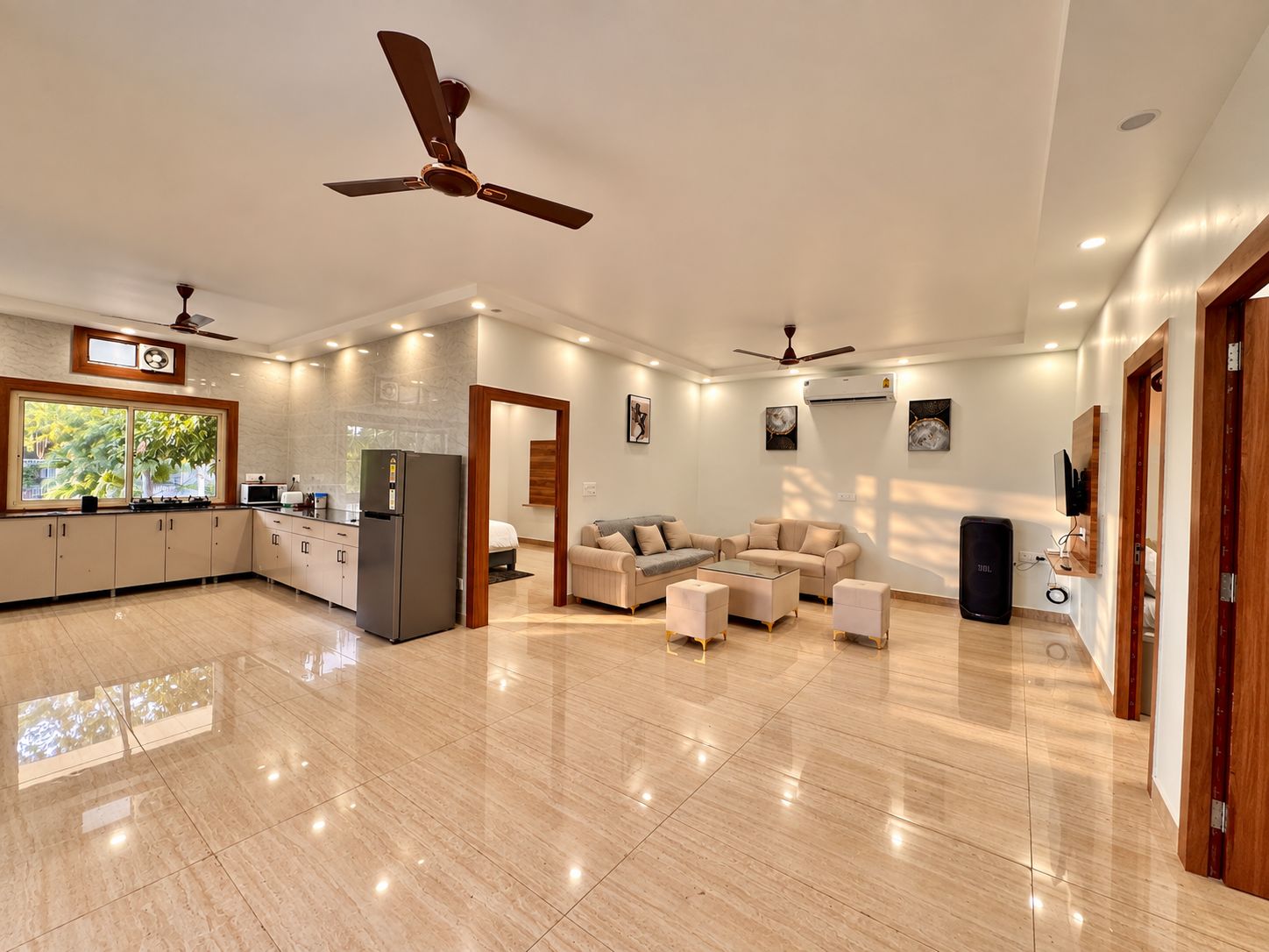 A spacious living area with a kitchen, a dining table, and a seating area with sofas. There are ceiling fans and recessed lighting.