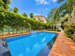 Una piscina rectangular con borde de baldosas, rodeada por una terraza de madera y abundante vegetación.