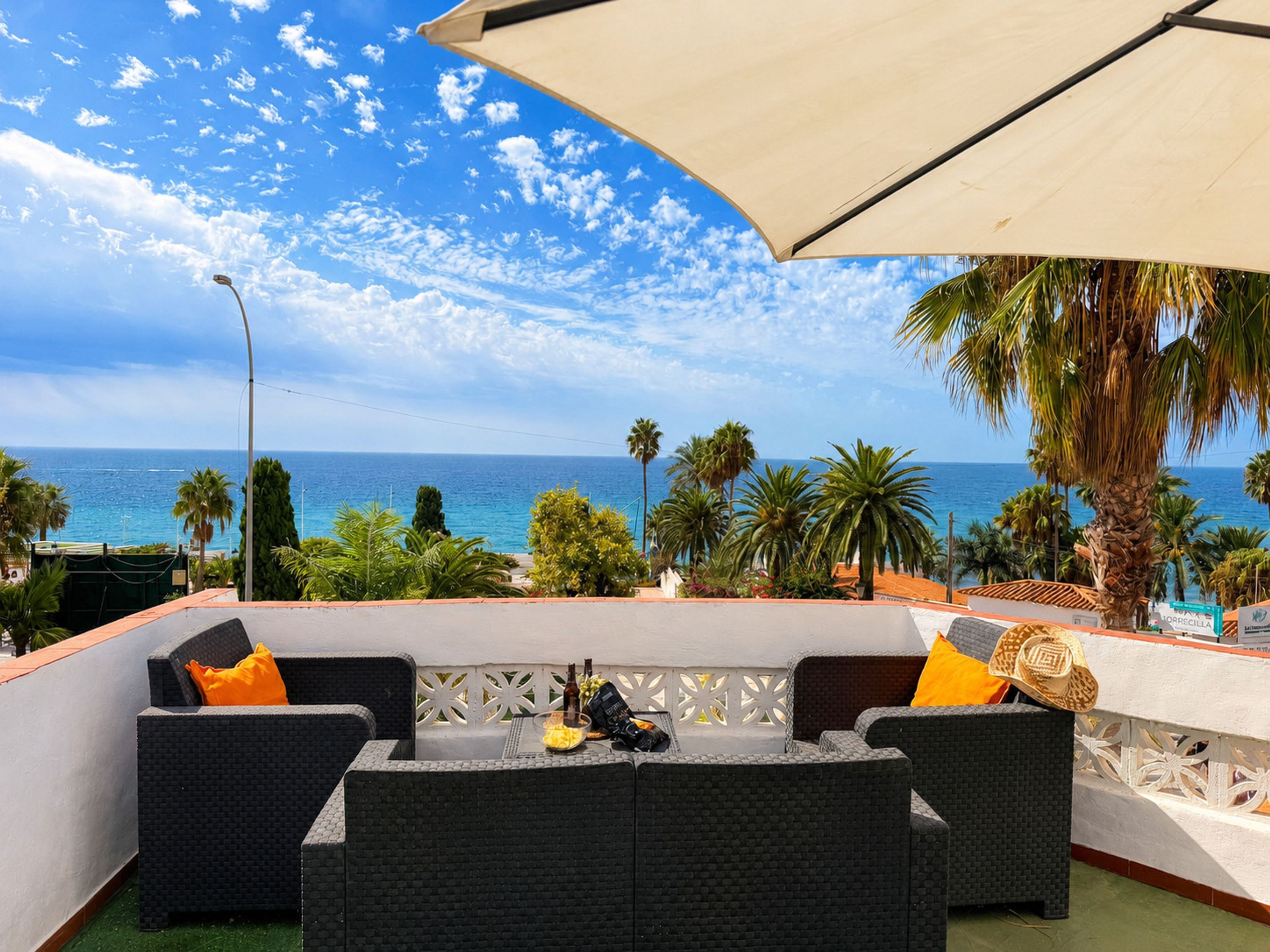 An outdoor seating area with wicker furniture, a table with bottles, and a view of the sea.
