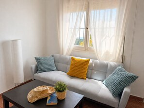 A living room with a sofa, cushions, a coffee table, a lamp, and a window with curtains. - Villa Juanita en Nerja con Vistas al mar (Nerja)
