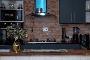 A kitchen with a brick wall, a gas stove, a coffee maker, and a vase with dried flowers on the counter.