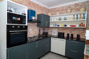 Eine Küche mit einer Wandverkleidung aus Ziegelsteinen, einem eingebauten Backofen, einer Kaffeemaschine und verschiedenen Küchenutensilien auf Regalen.