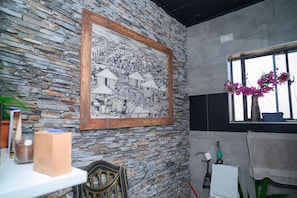 A room with a stone wall, a framed black and white photograph, a window with flowers, and a chair. - Forest Hill House - 2 Bedroom Villa in New Kasama (Lusaka)