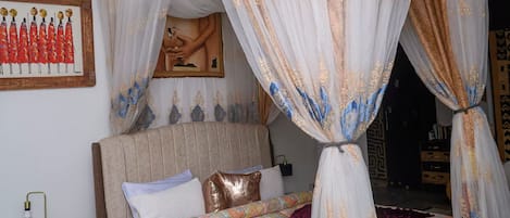 A bedroom with a four-poster canopy bed, a nightstand with a lamp, a framed picture on the wall, and a patterned bedspread.
