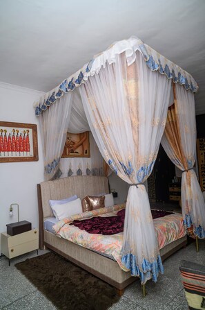 A bedroom with a four-poster canopy bed, a nightstand with a lamp, a framed picture on the wall, and a patterned bedspread. - Forest Hill House - 2 Bedroom Villa in New Kasama (Lusaka)