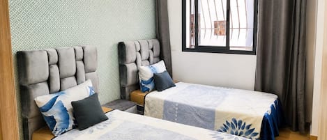 A room with two beds, a window with curtains, and a patterned wall.